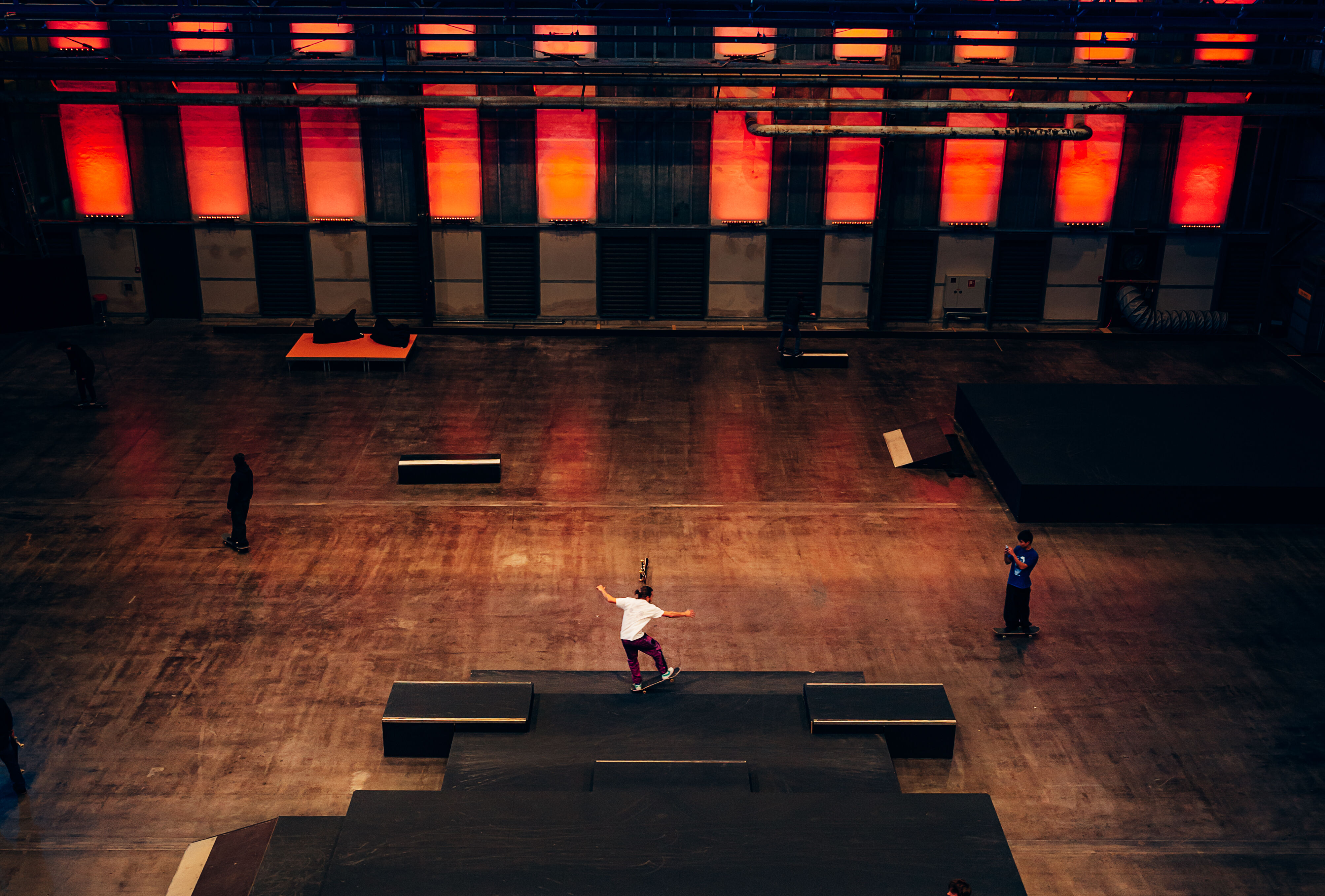 Skater auf einem Ostacle in der ansonsten leere Halle 3 der Jahrhunderthalle Bochum. Die Fensterfront ist rot beleuchtet.
